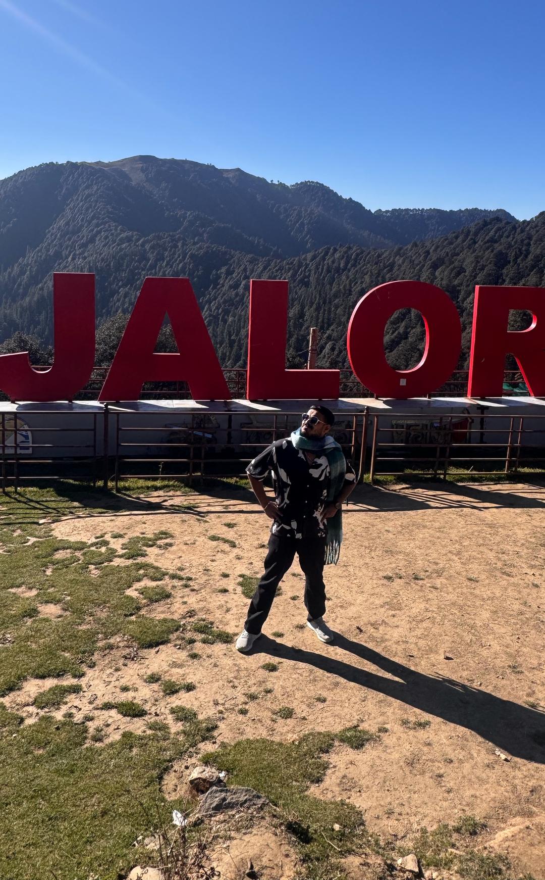 A guest at the Jalori Pass sign with Himalayan ridges behind